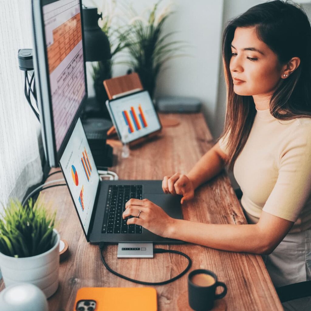 A woman working at a desk with multiple screens displaying data and charts, signifying IT virtual assistant services.