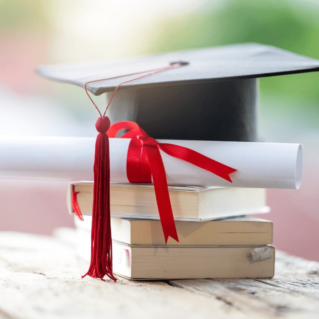 An image of a graduation cap and diploma sitting atop a stack of books, symbolizing academic workbooks creation services.