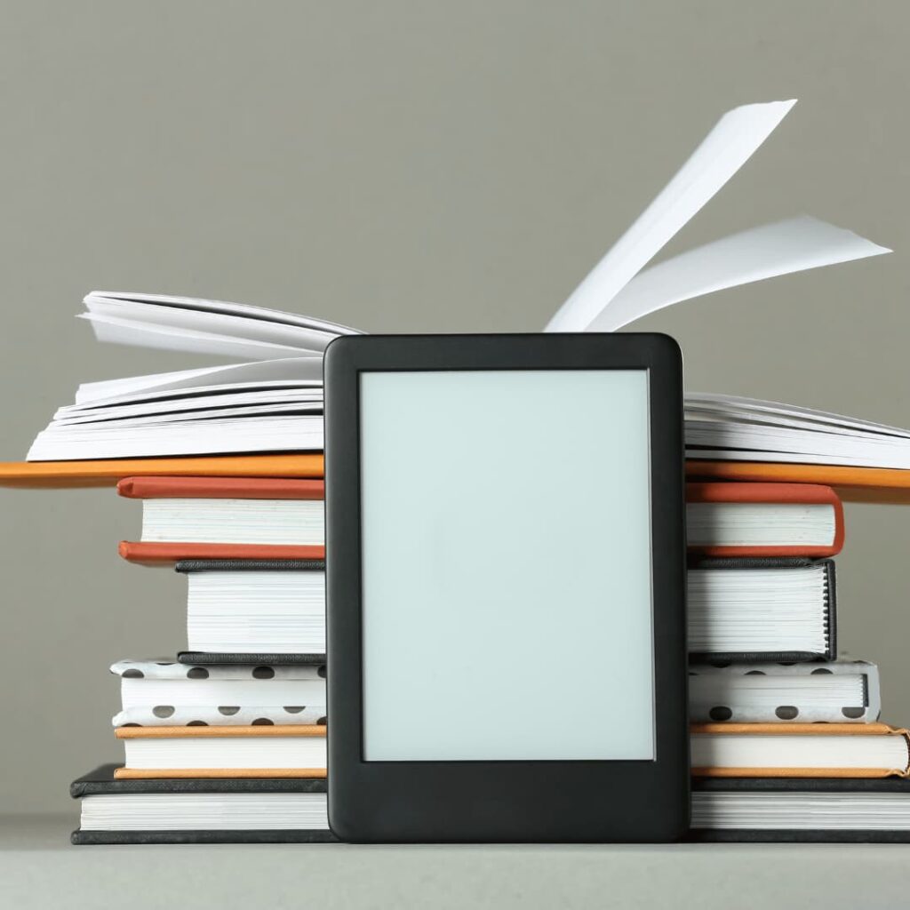 An image of a digital eBook reader surrounded by paper books, highlighting digital workbooks creation services.