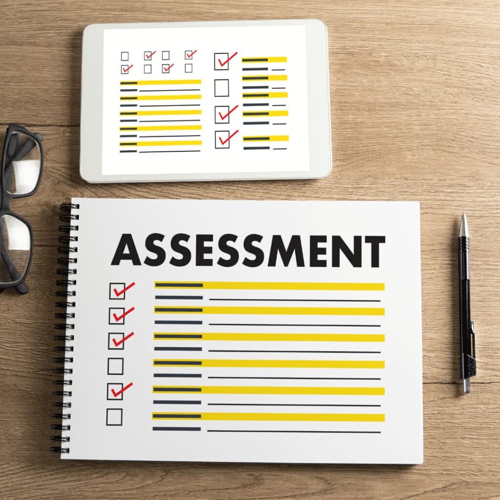 A tablet and a notebook with checklists, glasses, and a pen on a wooden table, highlighting educational assessment creation services.