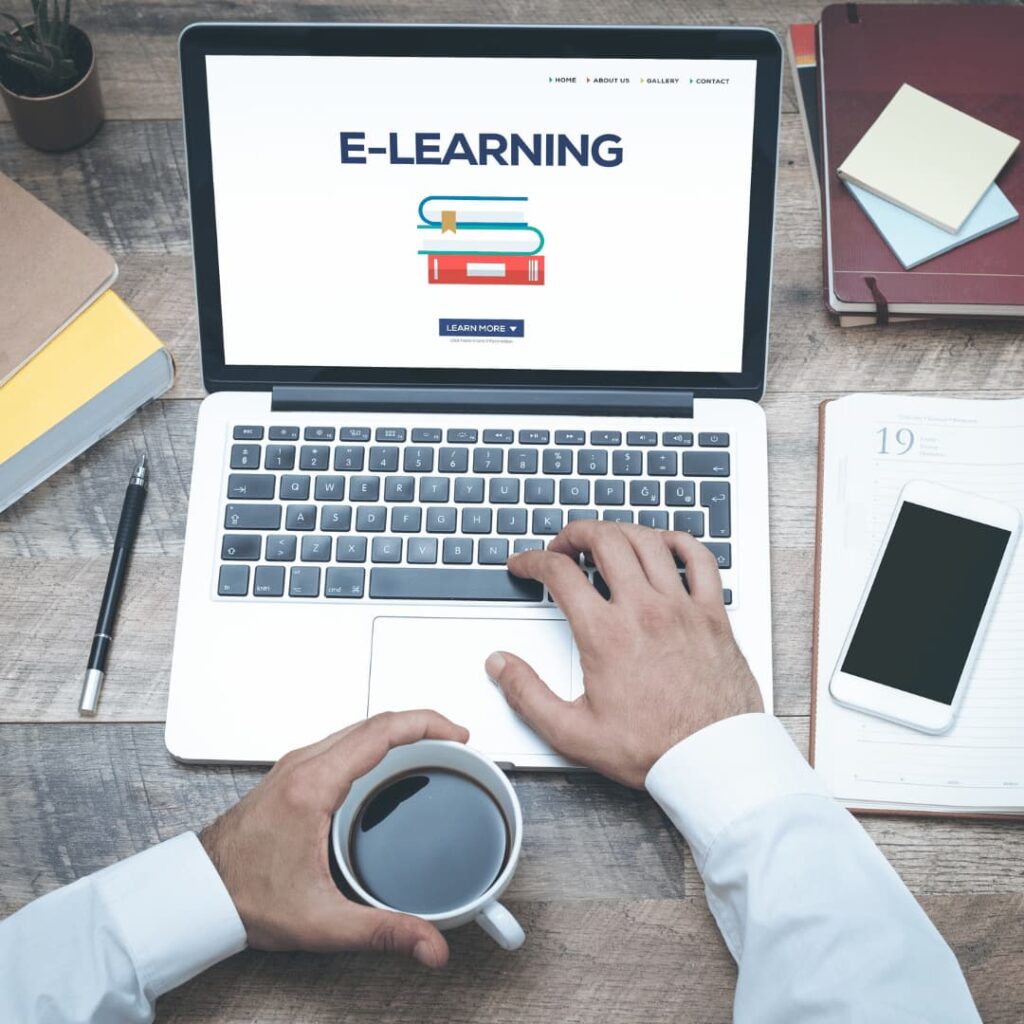 A person working on a laptop with an 'E-Learning' interface, surrounded by educational materials, signifying the instructional design and eLearning modules creation services.