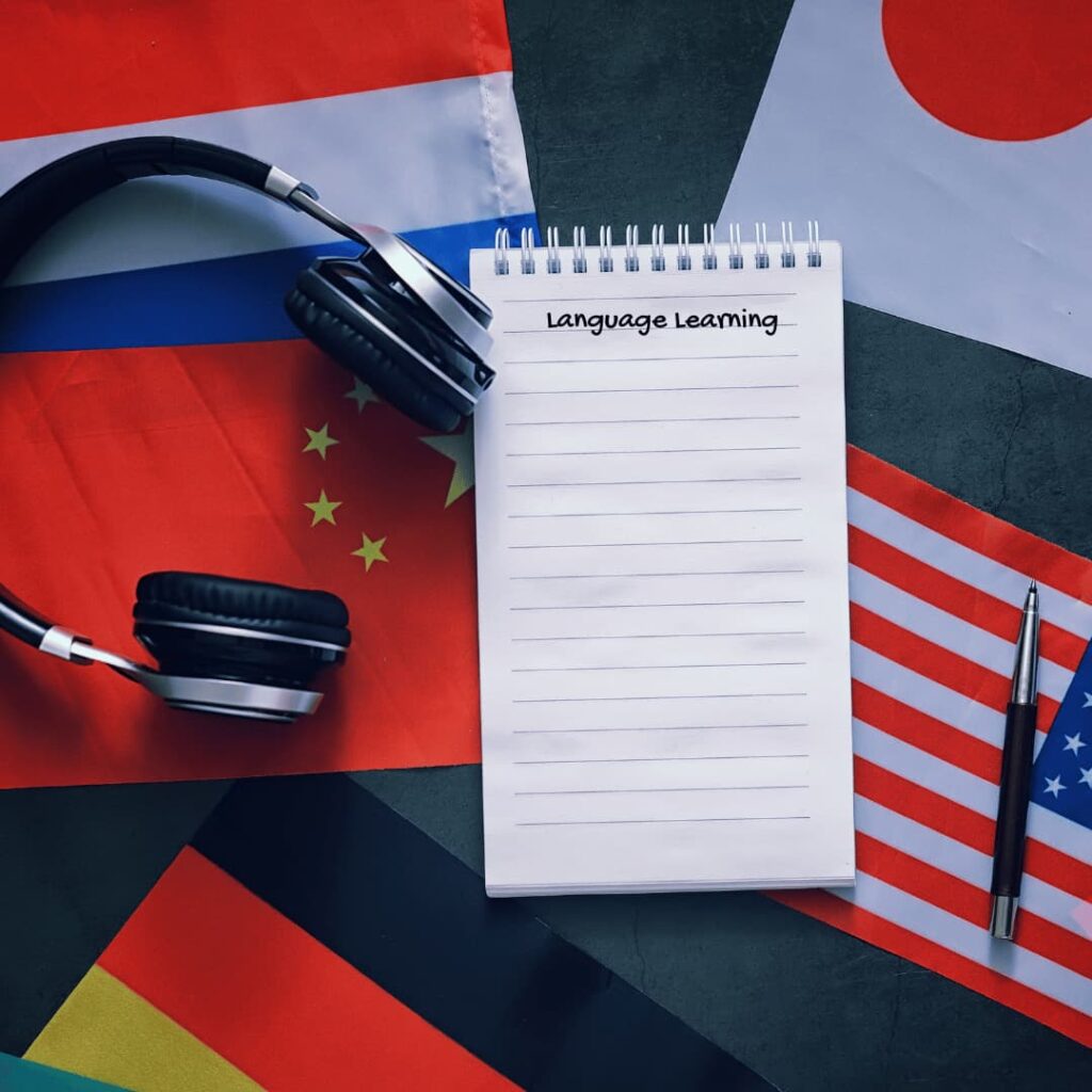 A notepad with "Language Learning" written on it, placed alongside international flags and headphones, symbolizing language learning workbooks creation services.