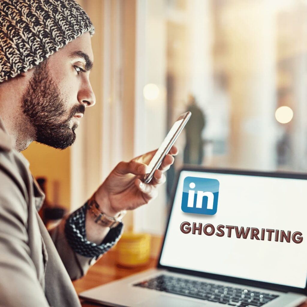 A man in a beanie and glasses using a smartphone while a laptop screen displays 'LinkedIn GHOSTWRITING,' indicating LinkedIn ghostwriting services.