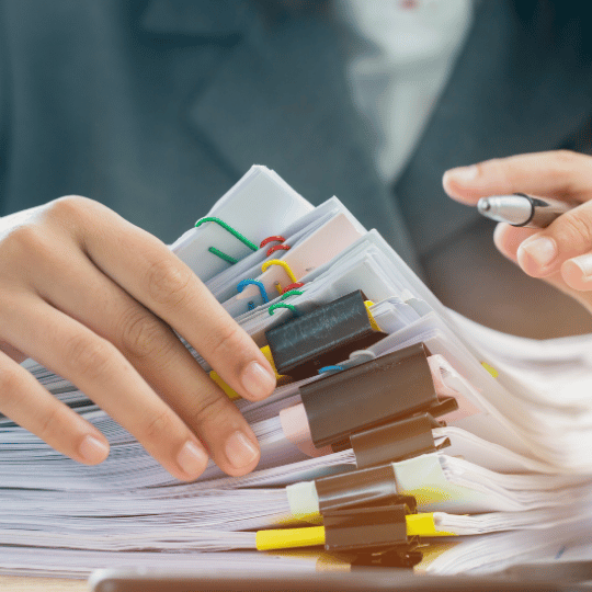 A close-up of a person's hands organizing stacks of papers with various colored paper clips, depicting the detailed nature of research paper writing, indicating research paper writing services.