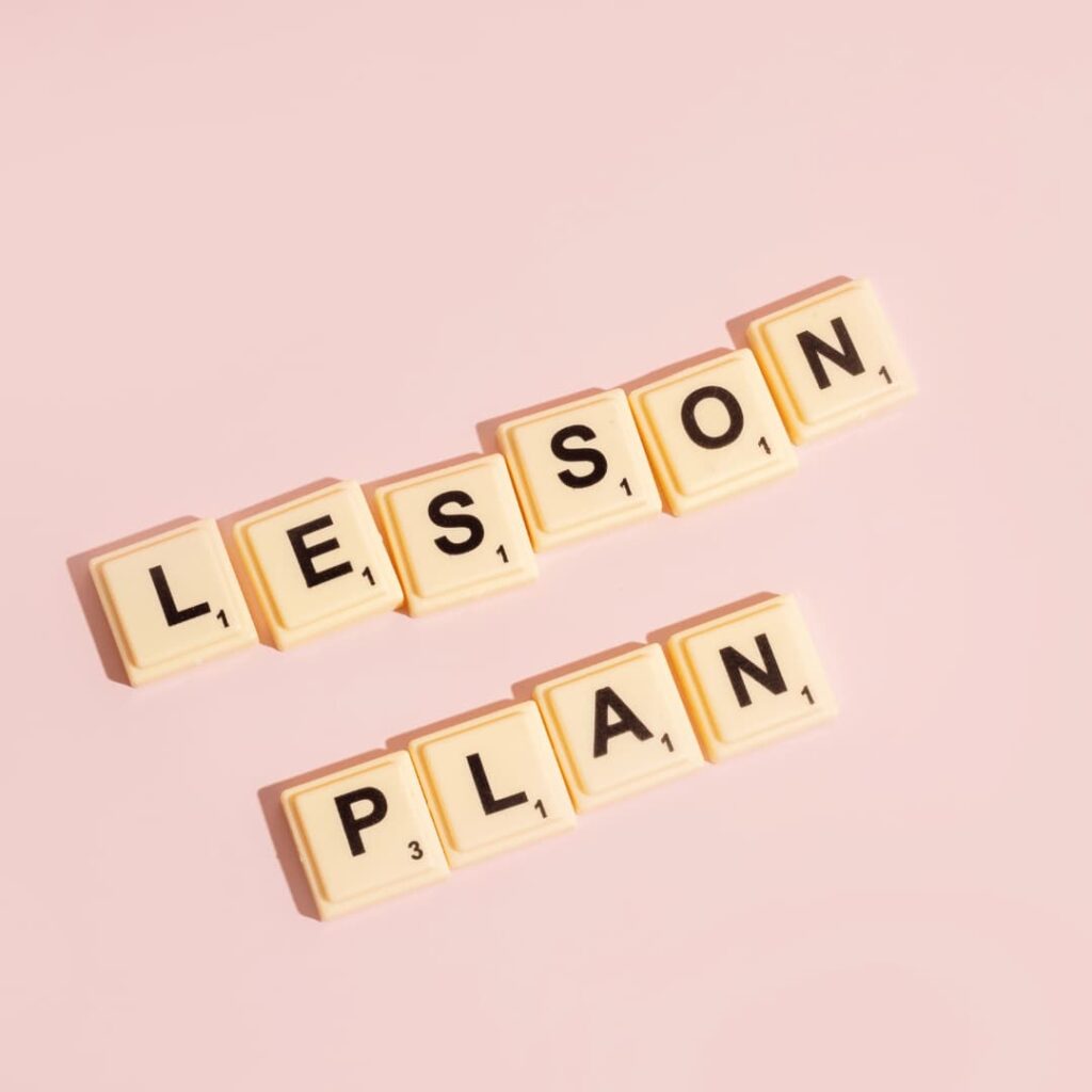 Scrabble tiles arranged to spell "LESSON PLAN" on a light pink background, representing standard lesson plans creation services.