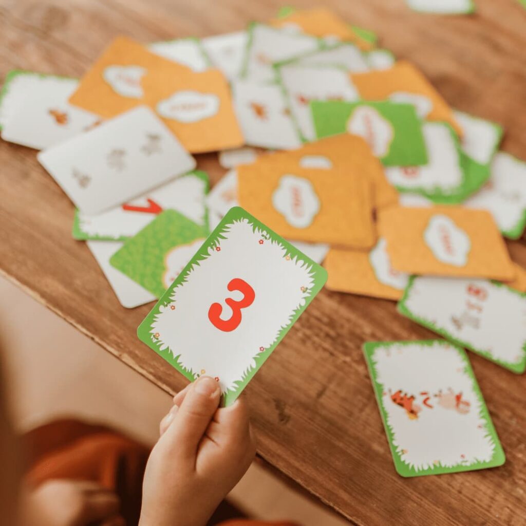 A hand holding a flashcard with the number 3 among other cards on a wooden table, representing traditional flashcards creation services.