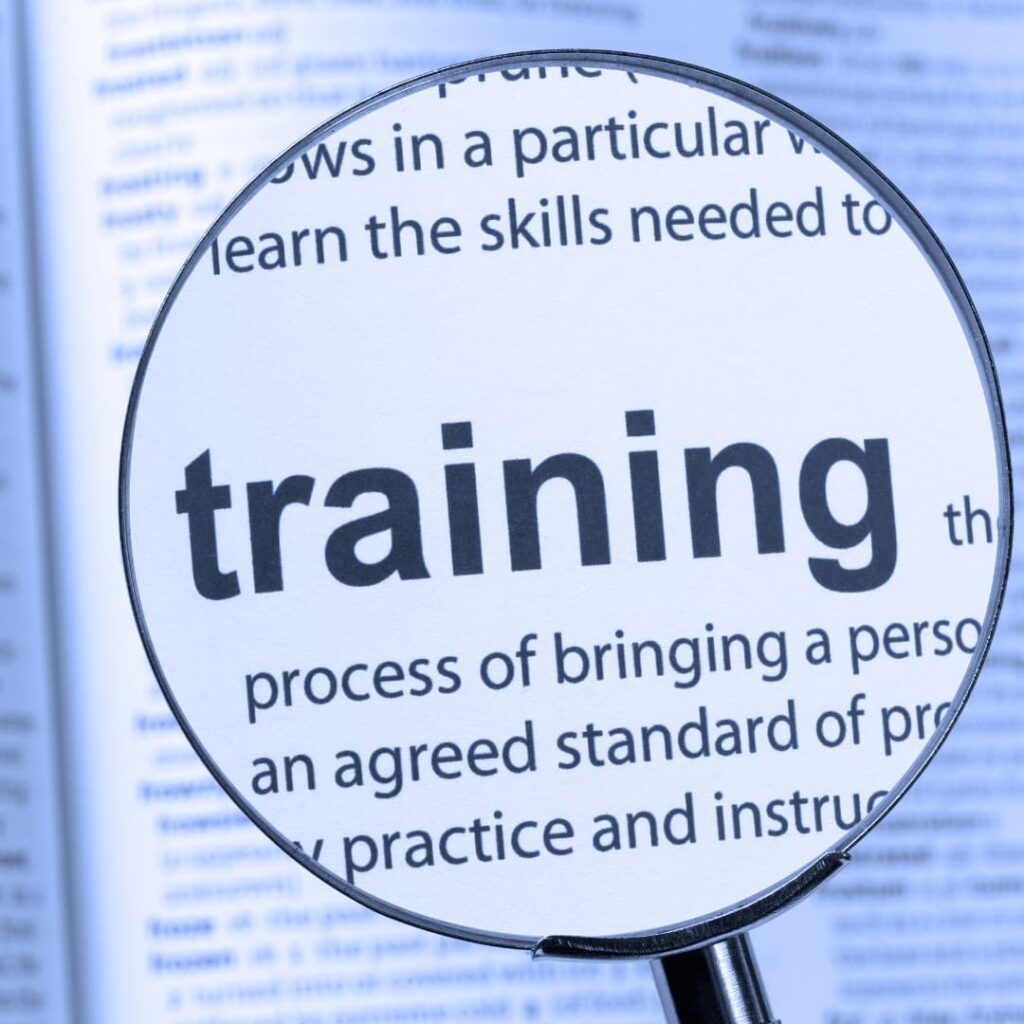 A magnifying glass focusing on the word "training" in a dictionary, symbolizing training workbooks creation services.