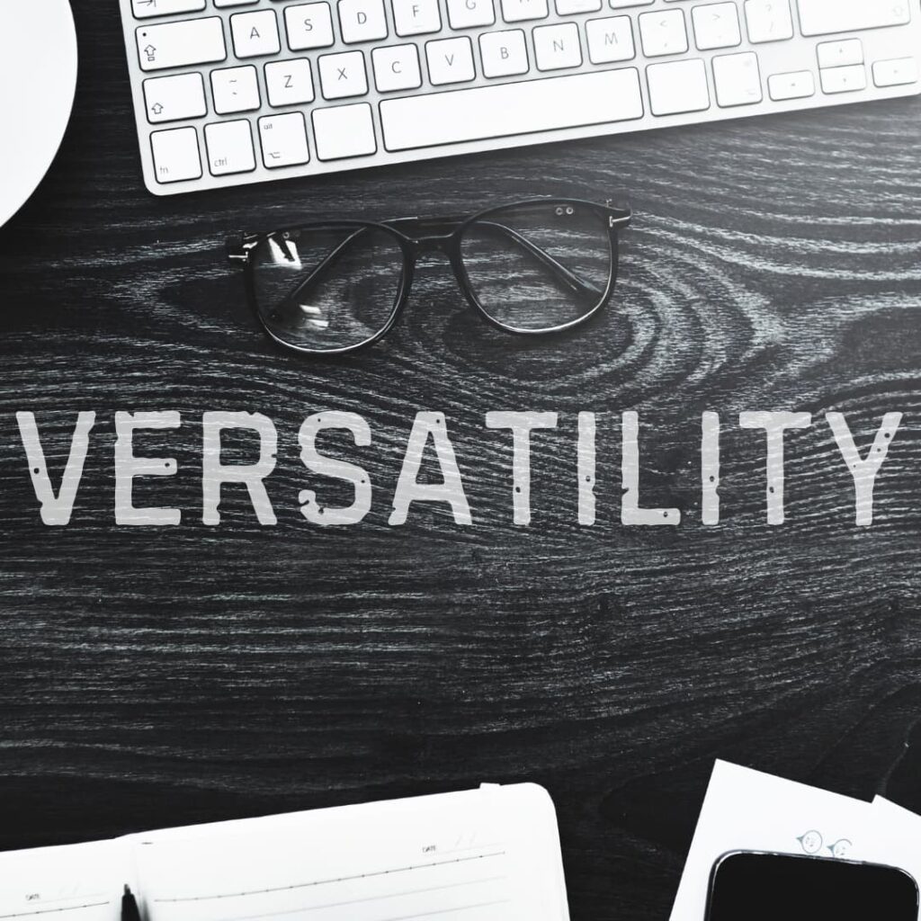 A workspace with glasses, a keyboard, and the word "VERSATILITY" on a wooden surface, representing versatility and volume in custom K12 content development services.