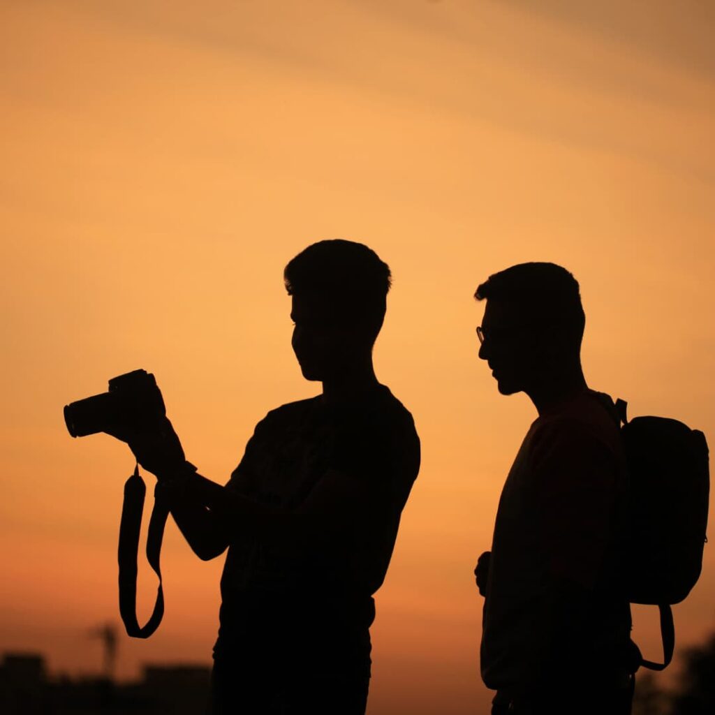 Silhouette of two photographers reviewing a camera in front of a sunset, representing virtual assistant services for photographers.